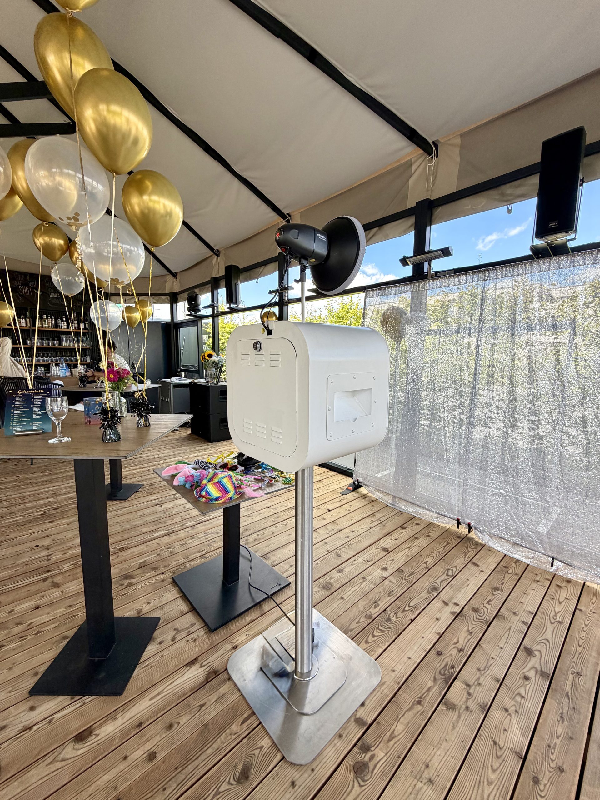 Rückansicht der weißen Fotobox Lite mit Studioblitz vor einem silbernen Fotohintergrund und goldenen Ballons in der Holzapfel Bar Kelkheim